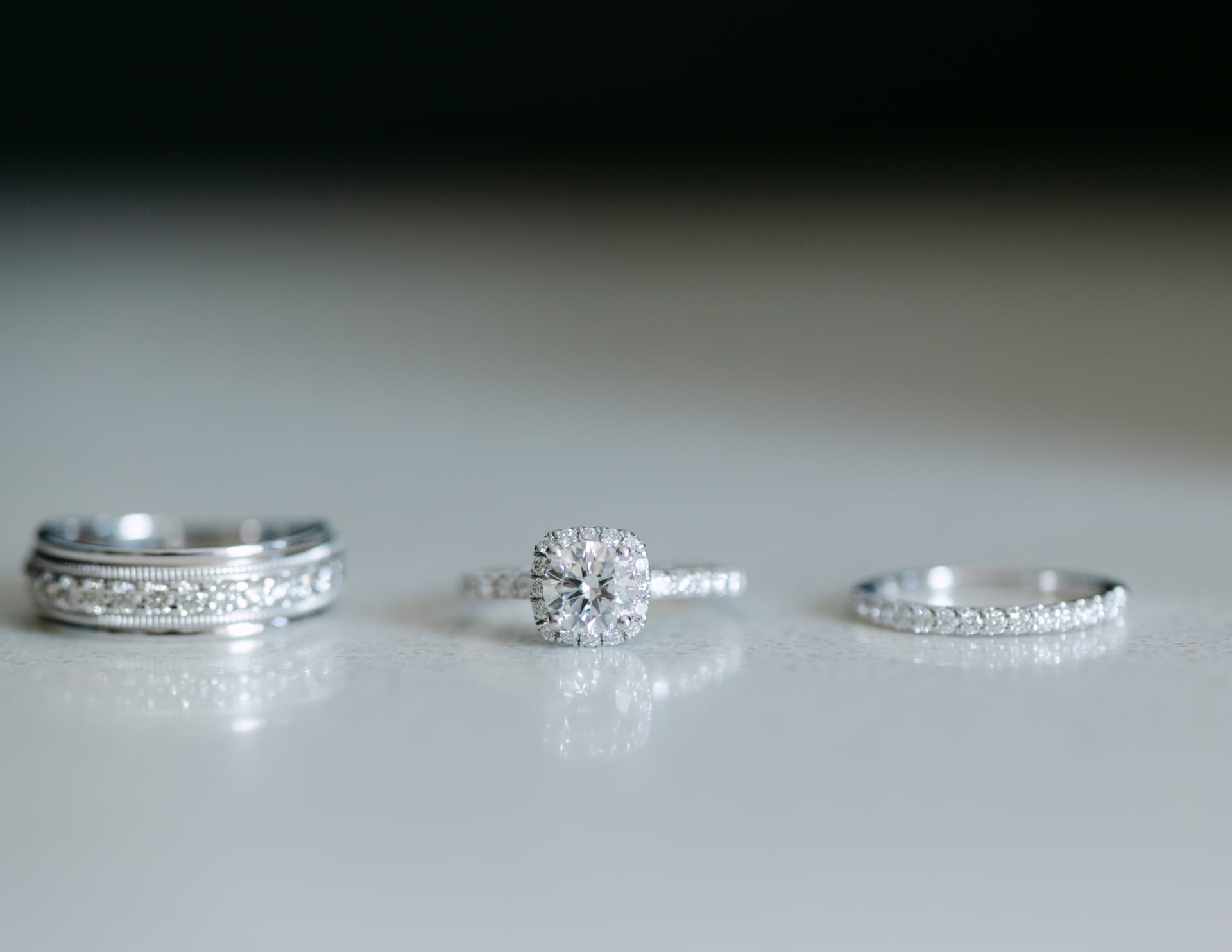 Engagement ring and wedding bands standing on a reflective surface