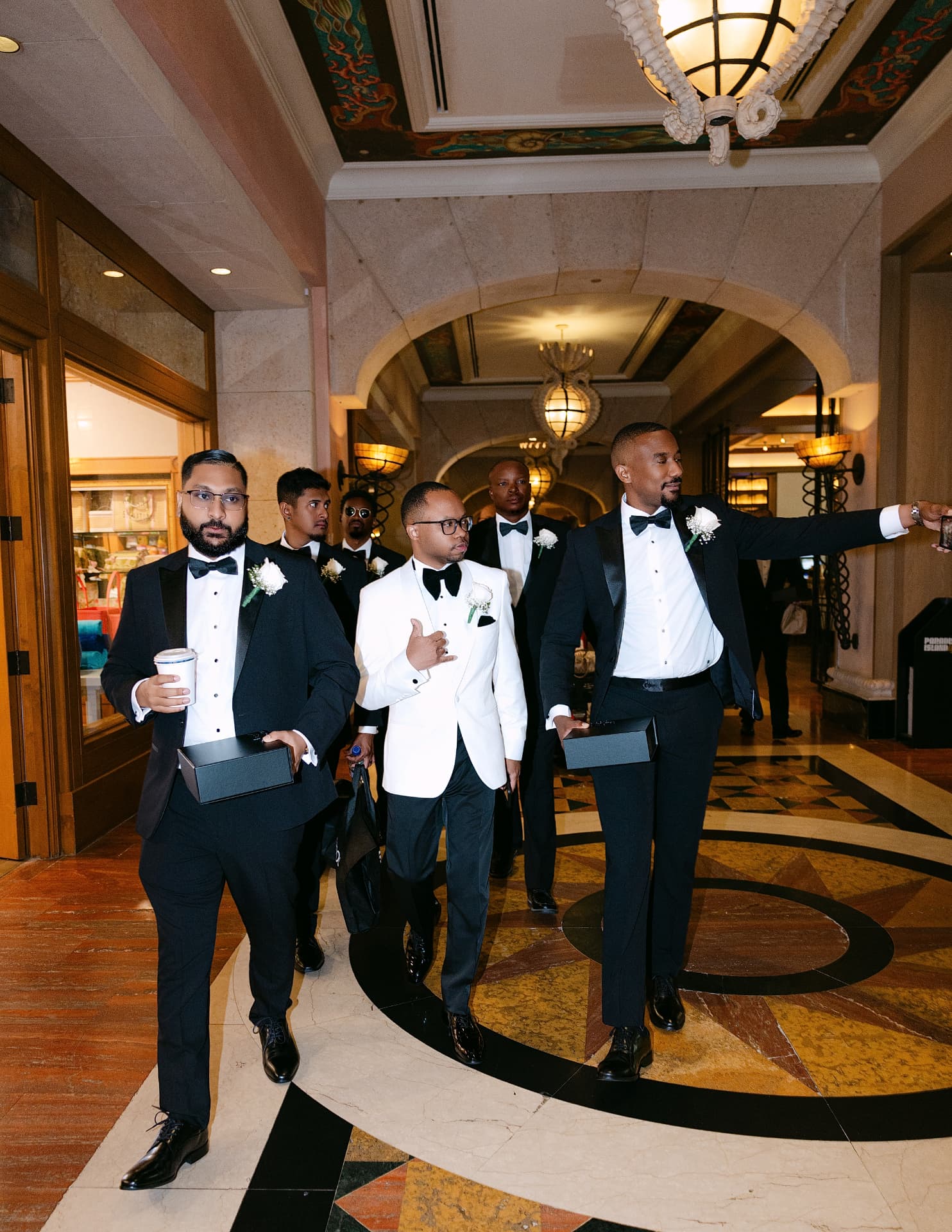 Groom and groomsmen in tuxedos walking through a grand lobby
