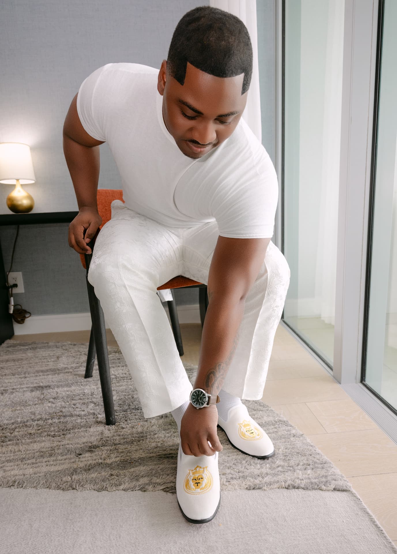 Groom in white lace trousers slipping on embroidered white loafers