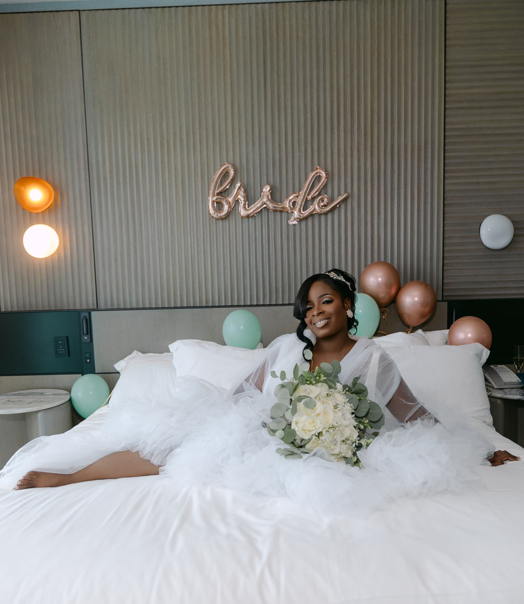 Bride reclining on a bed with her bouquet and balloons behind her