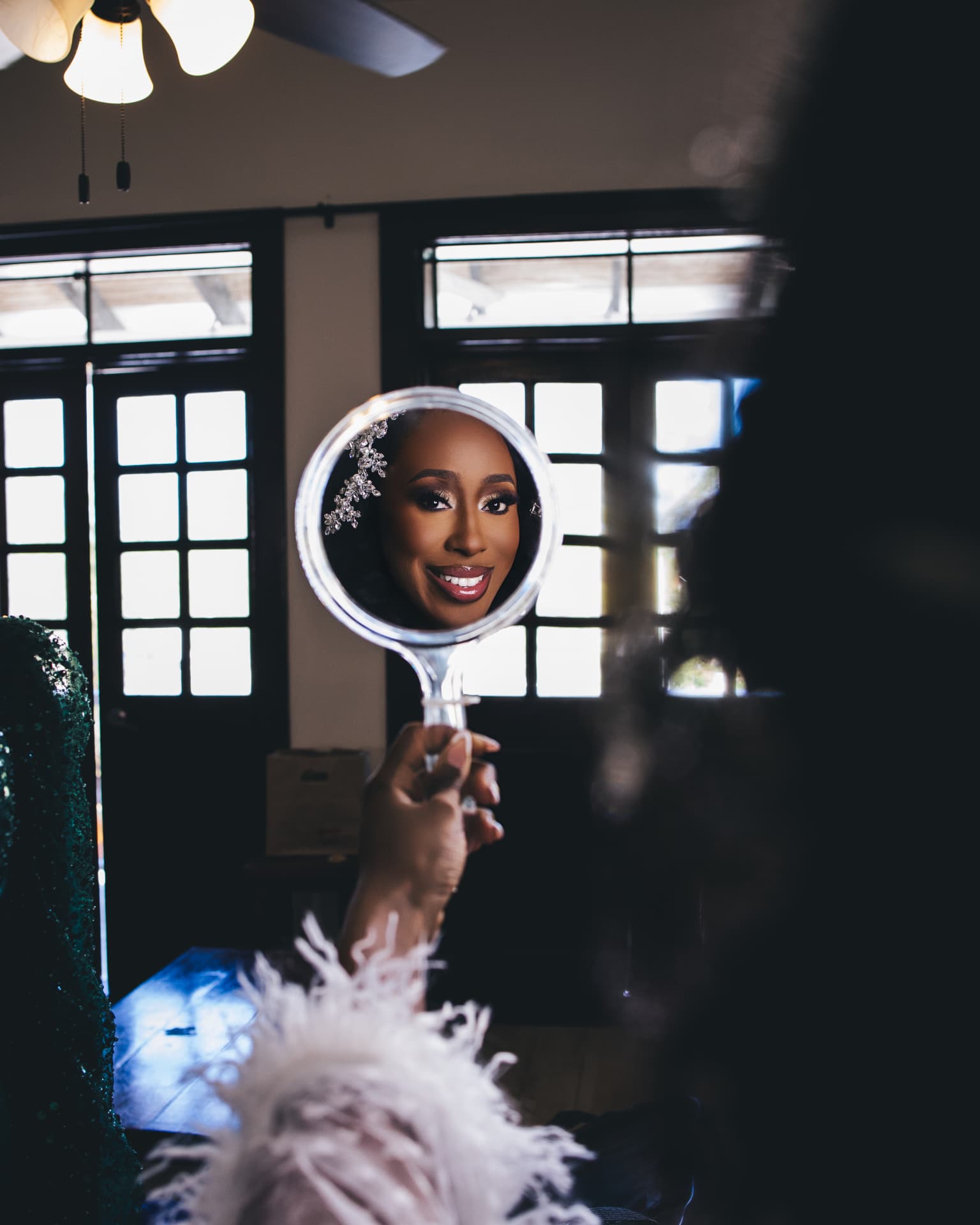 Bride smiling at her reflection in a hand mirror, wearing a crystal headpiece