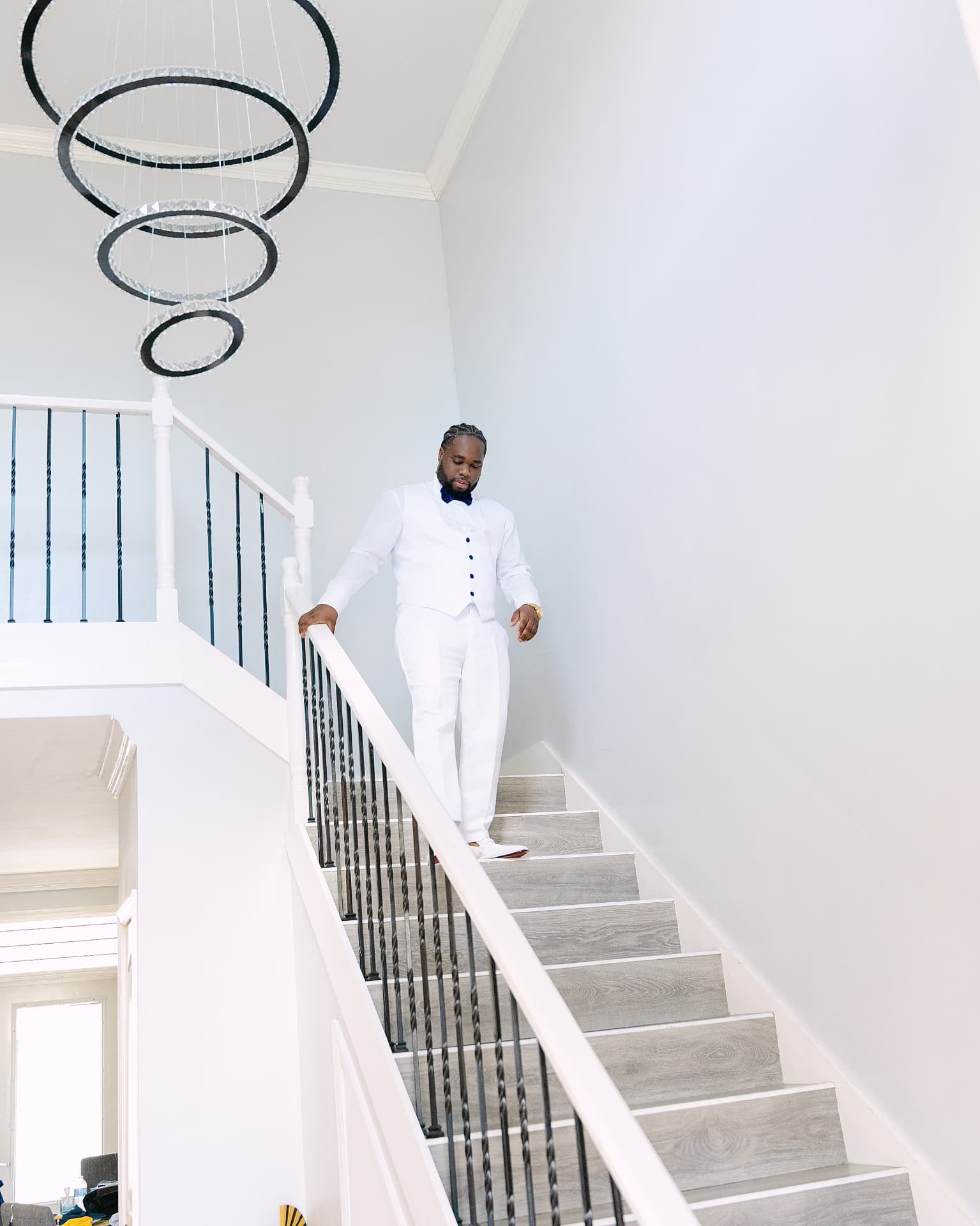 Groom in a white suit walking down a bright staircase