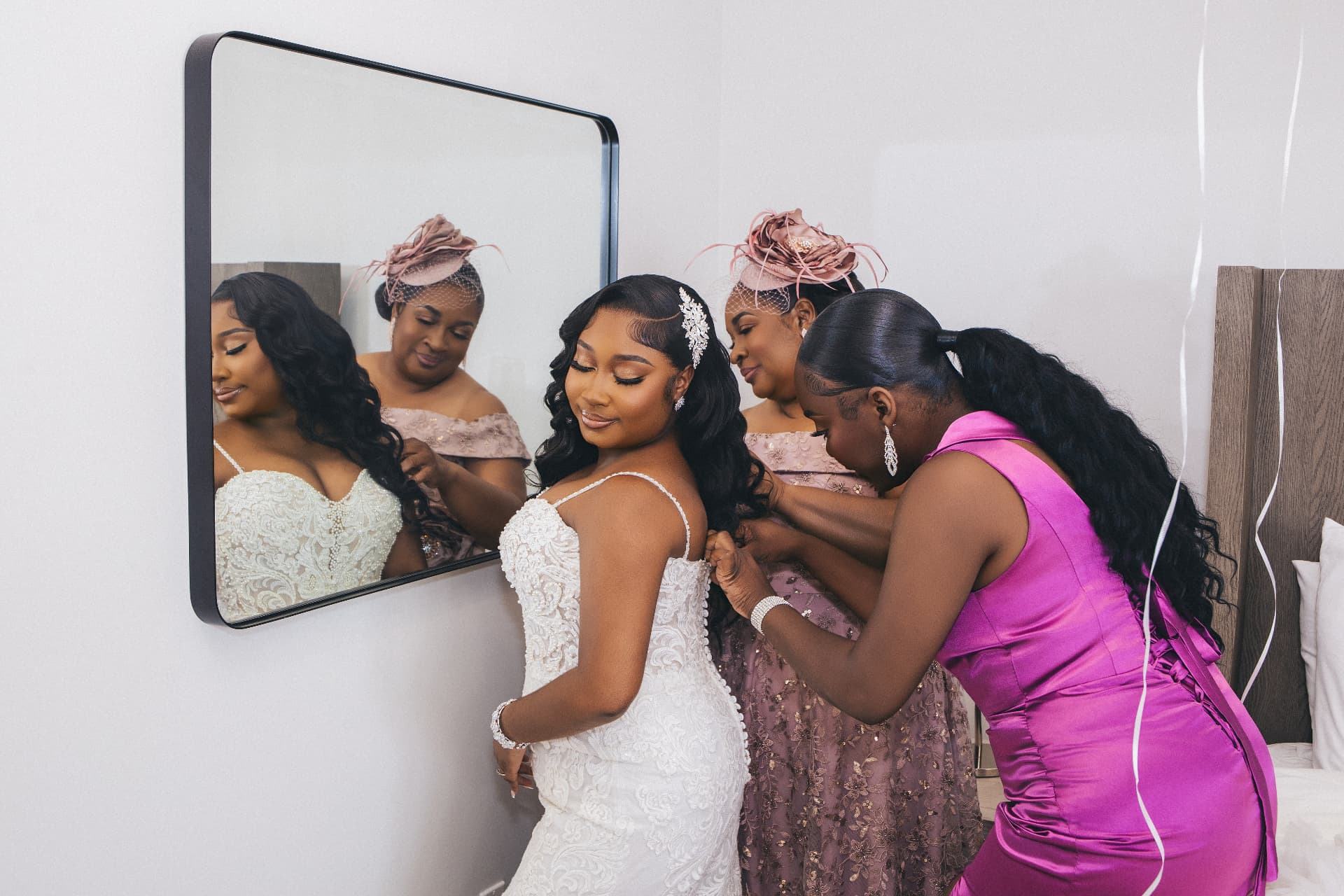 Gown being buttoned as the bride looks into a mirror