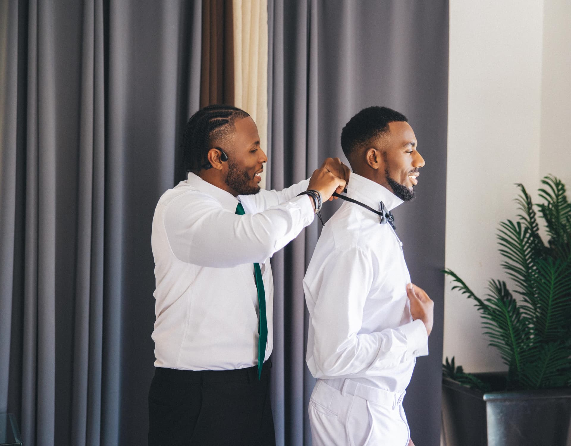 Groomsman fastening the groom's bow tie by a window