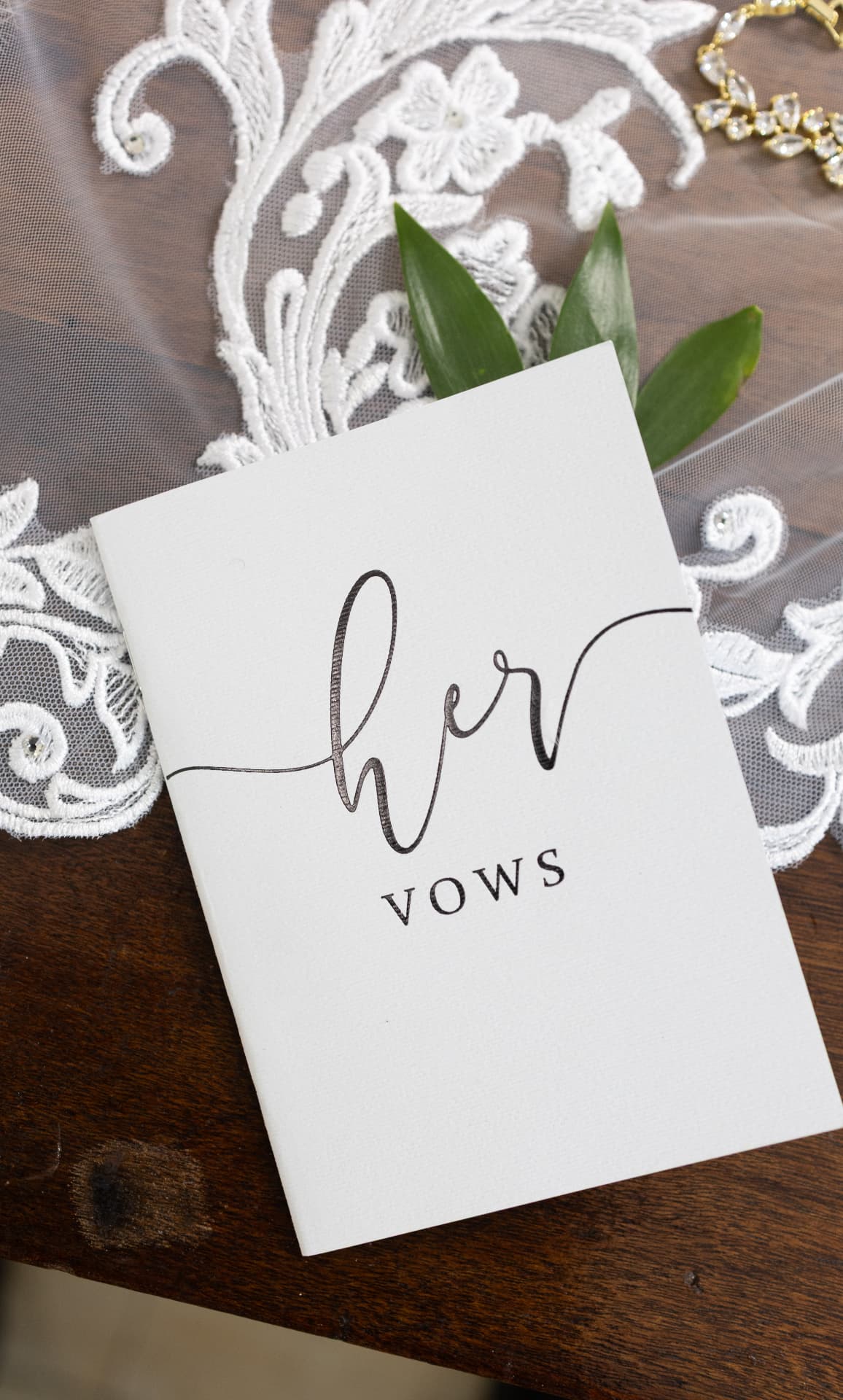 Her vow book on a veil with greenery and a crystal bracelet