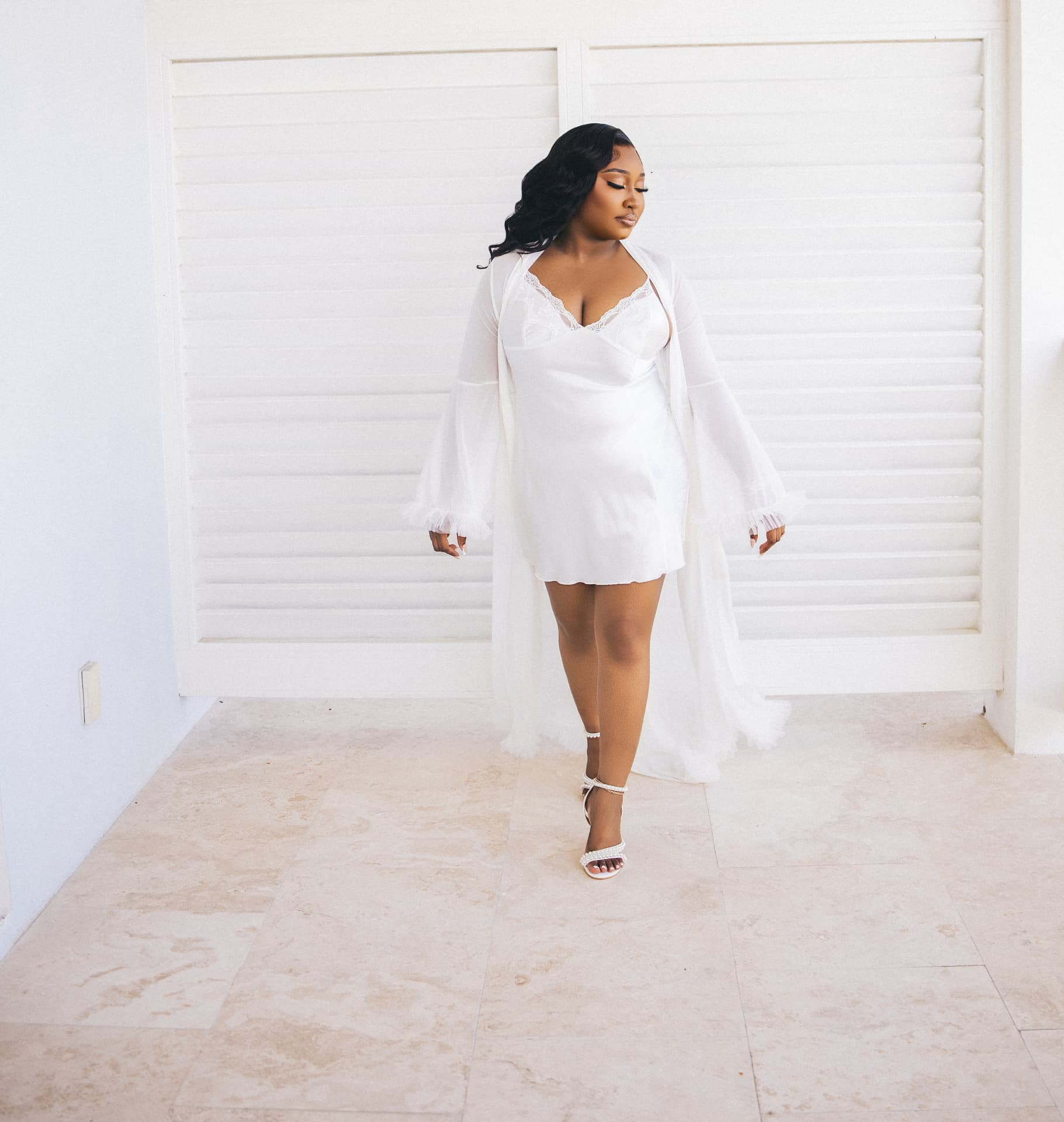 Bride walking in a slip and sheer robe against a bright white wall
