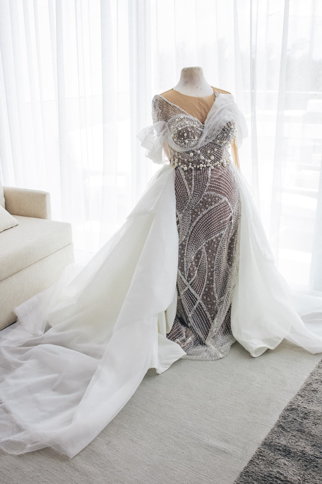 Beaded wedding gown displayed on a dress form by sheer curtains