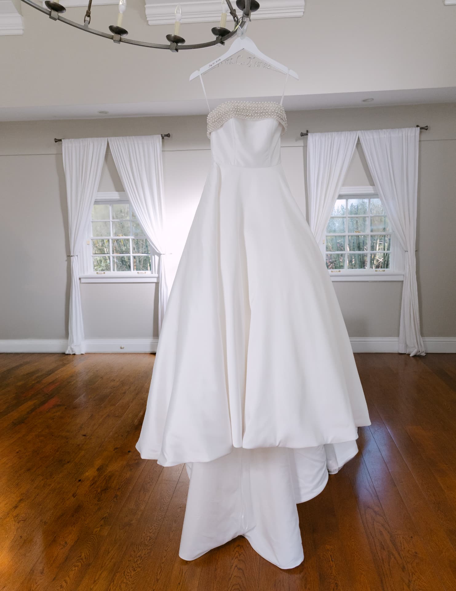 Ball gown hanging from a chandelier in a bright room with white curtains