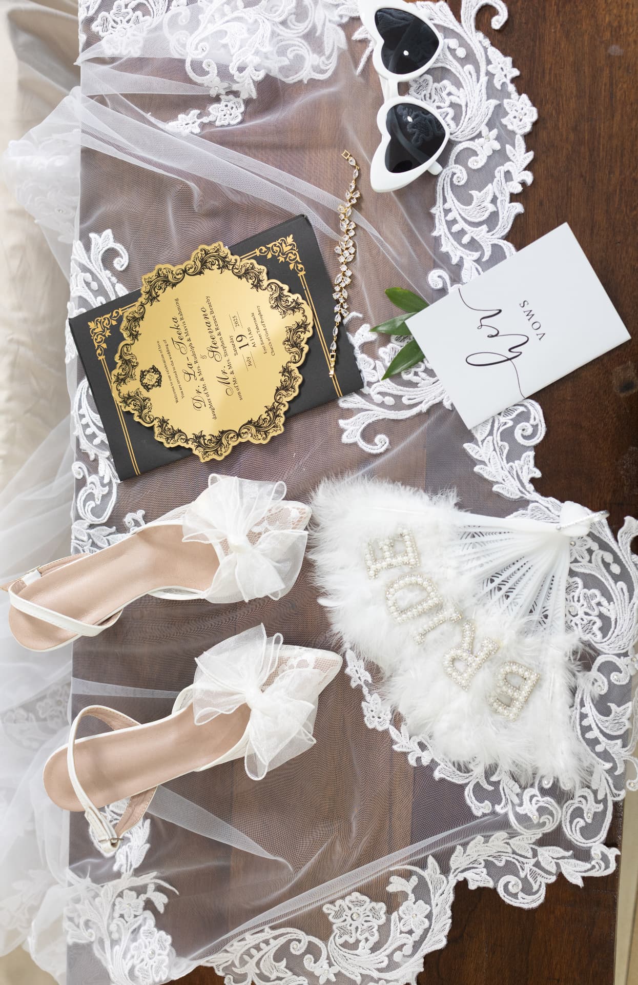 Gold and black invitation, vow book, bracelet, heels, and feather fan on a veil